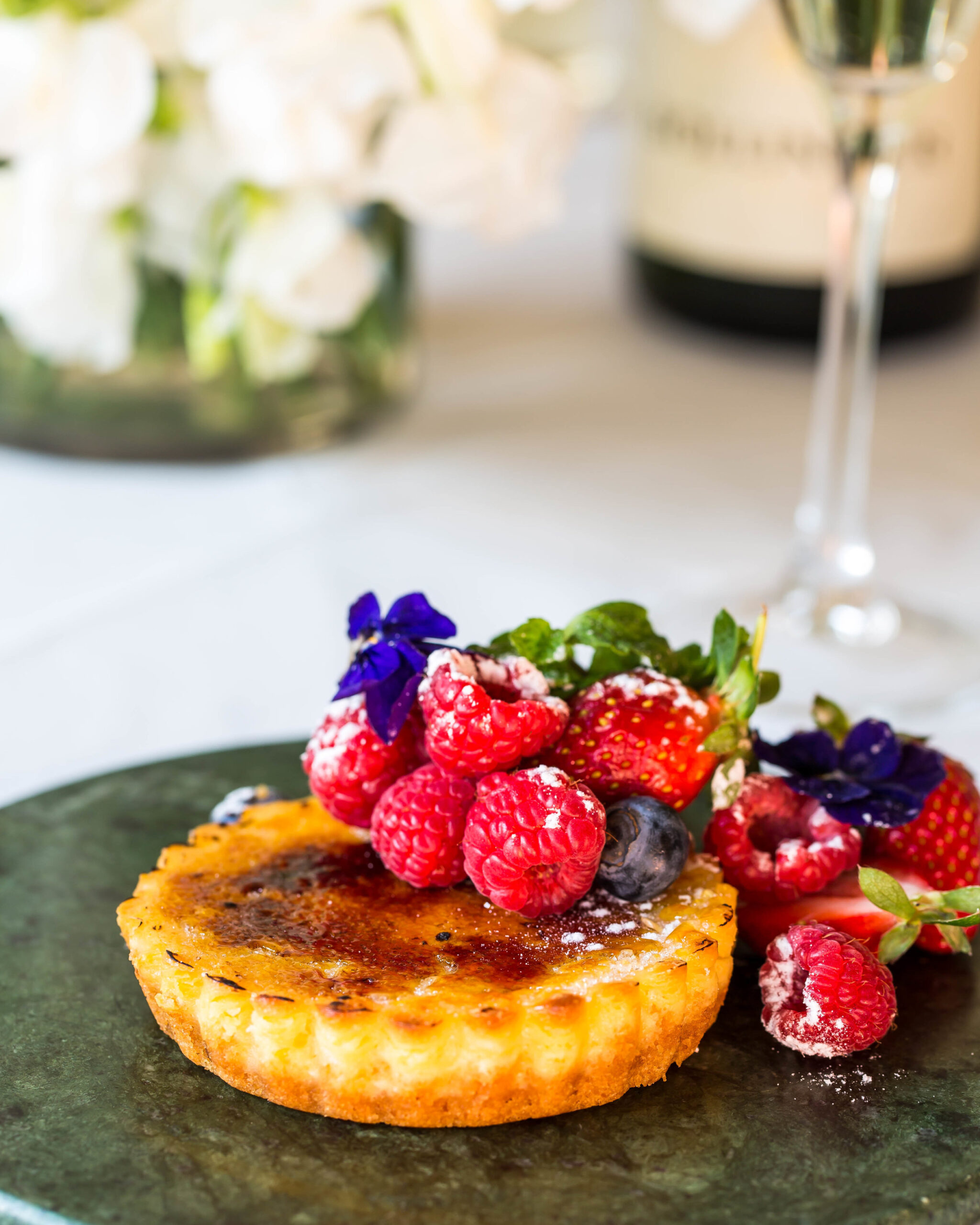 Crème brûlée tart topped with raspberries, strawberries and edible purple flowers