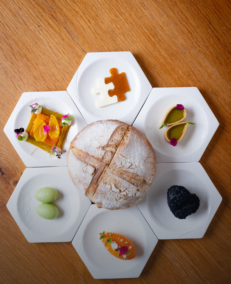 Rustic round loaf centered among six hexagonal plates of colorful small bites