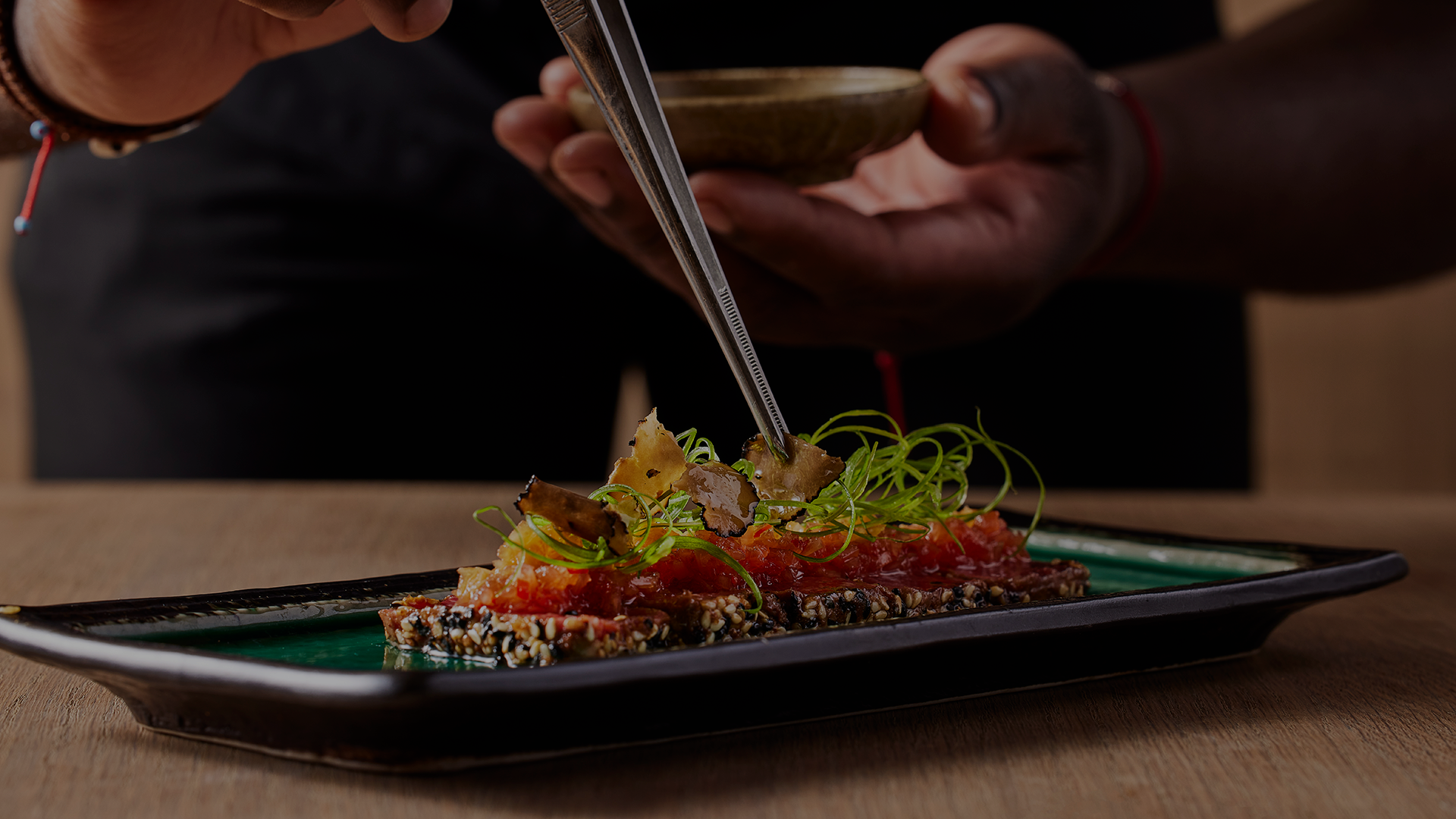 Chef plating raw fish tartare with microgreens on sesame-crusted toast