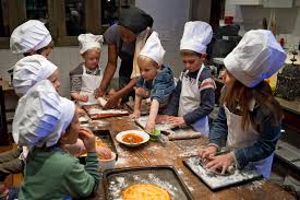 Children in chef hats making pizzas at a flour-dusted communal table