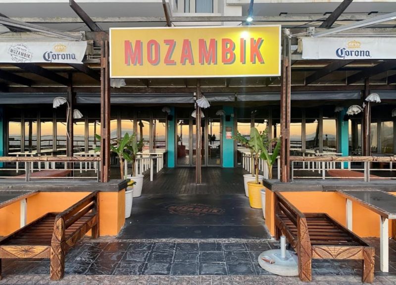 Mozambik restaurant entrance with empty outdoor seating and Corona umbrellas