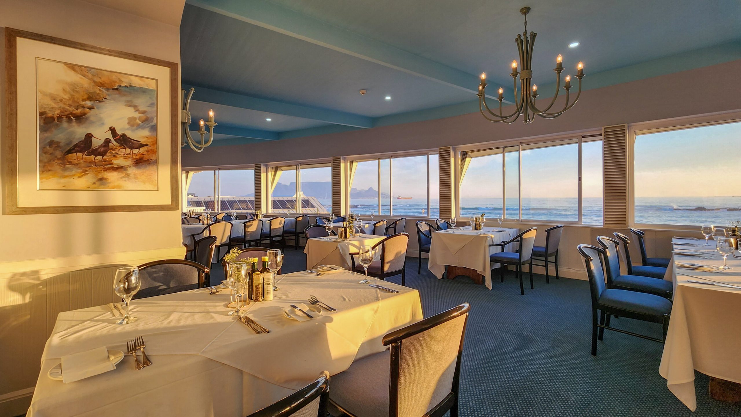 Ocean-view restaurant dining room with tables set at sunset