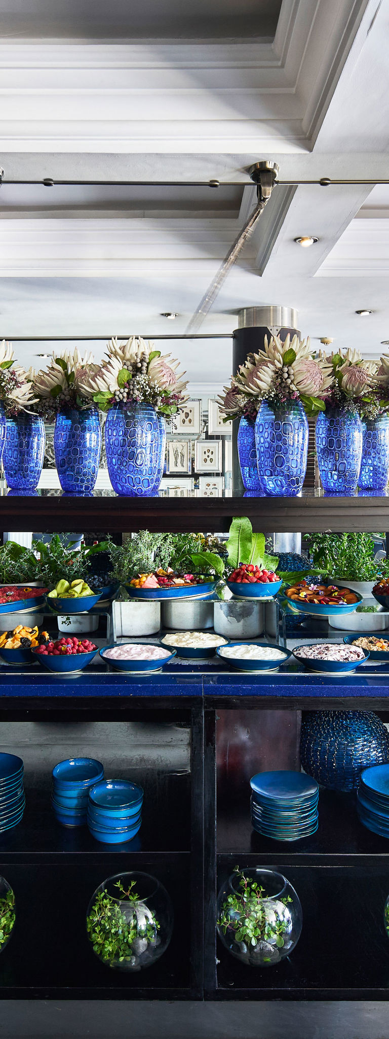 Buffet display with blue glass vases, bowls of salads, and stacked plates