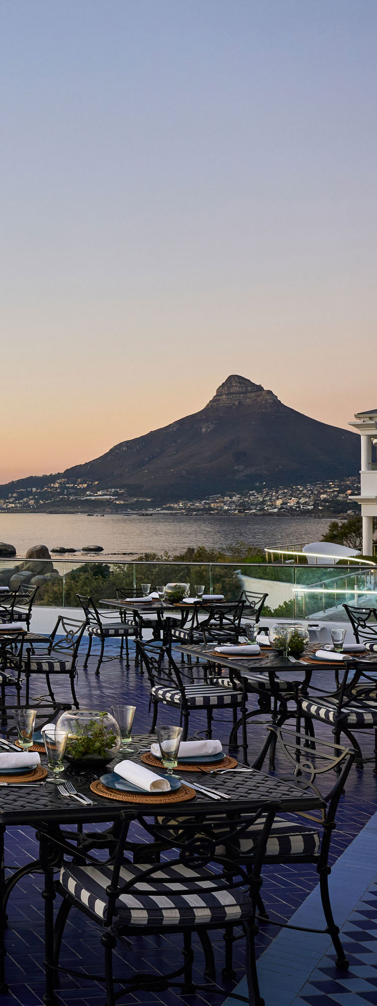 Outdoor terrace dining set overlooking sea and rocky mountain at sunset