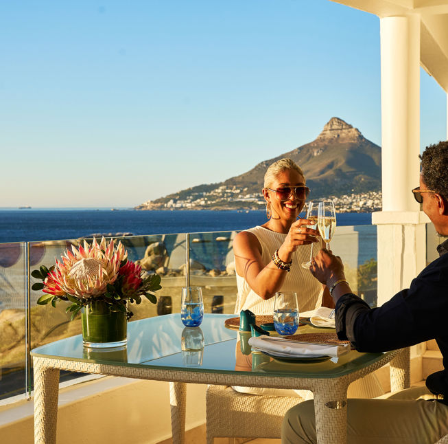 Couple toasting champagne on balcony overlooking ocean and mountain