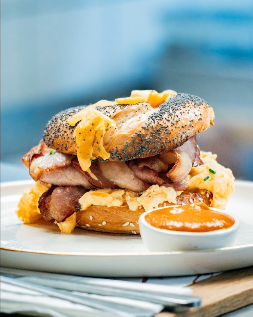 Poppy-seed bagel breakfast sandwich with bacon, scrambled eggs, cheese and orange dipping sauce
