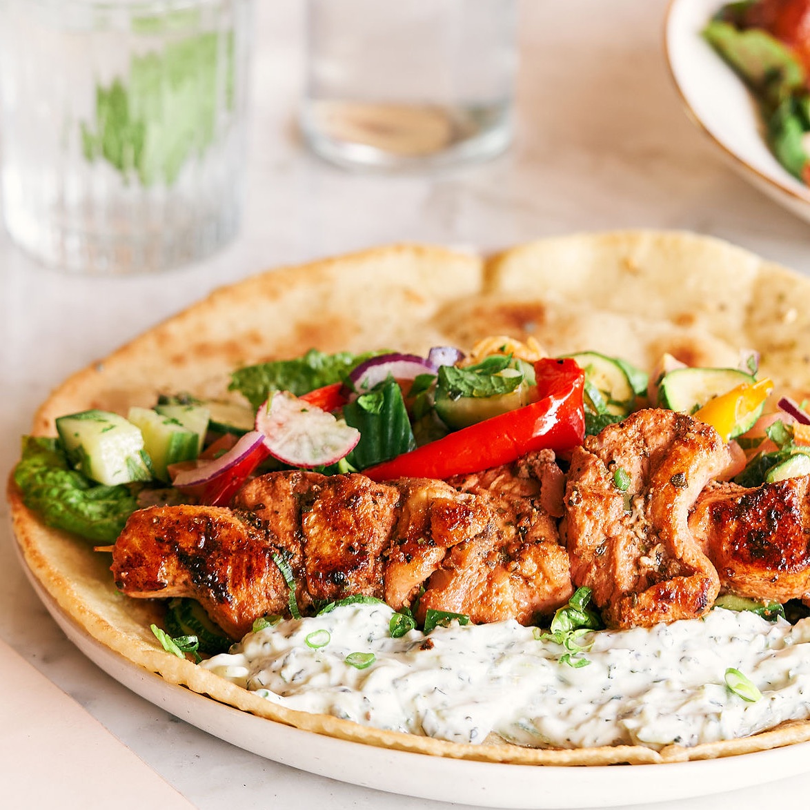 Grilled chicken kebab on flatbread with tzatziki and salad