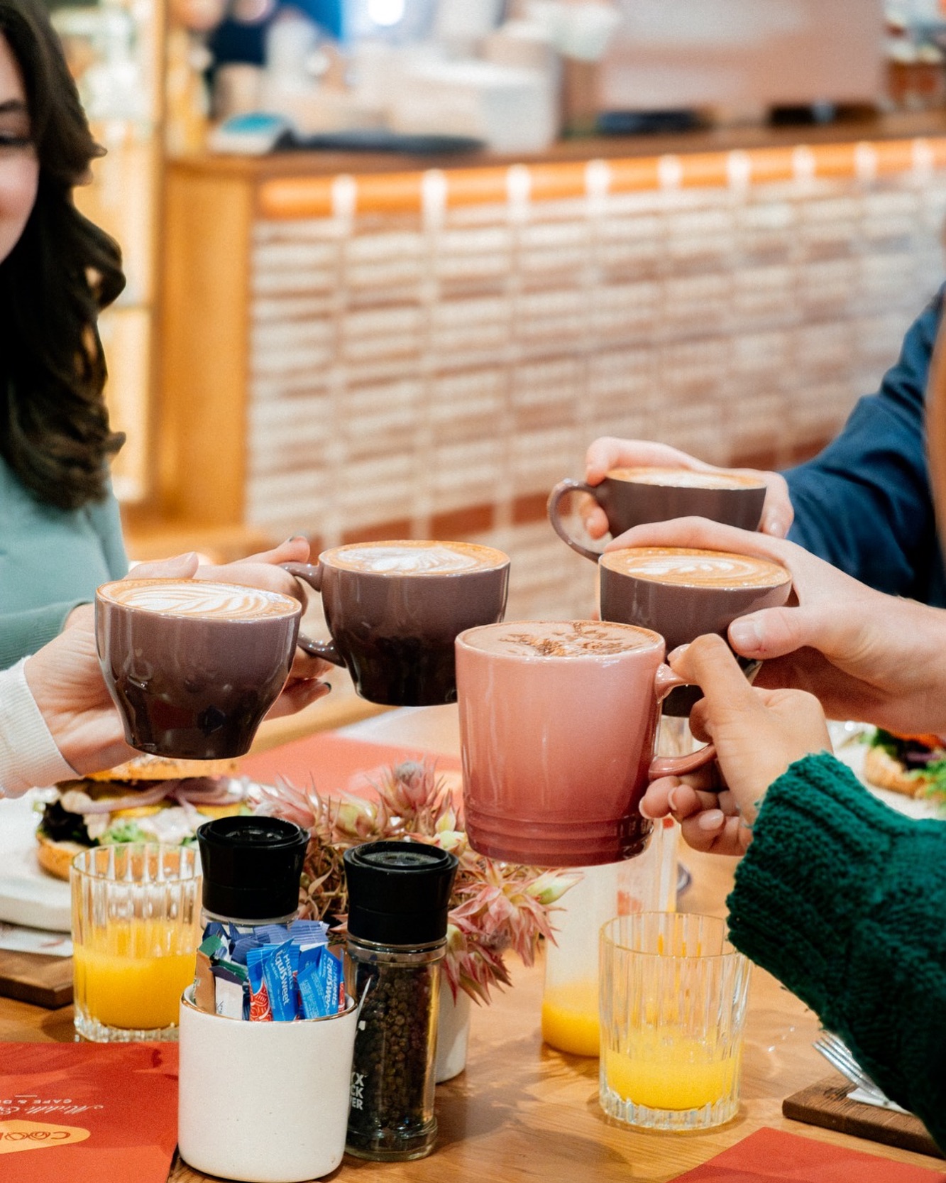 Four people clinking lattes over a breakfast table