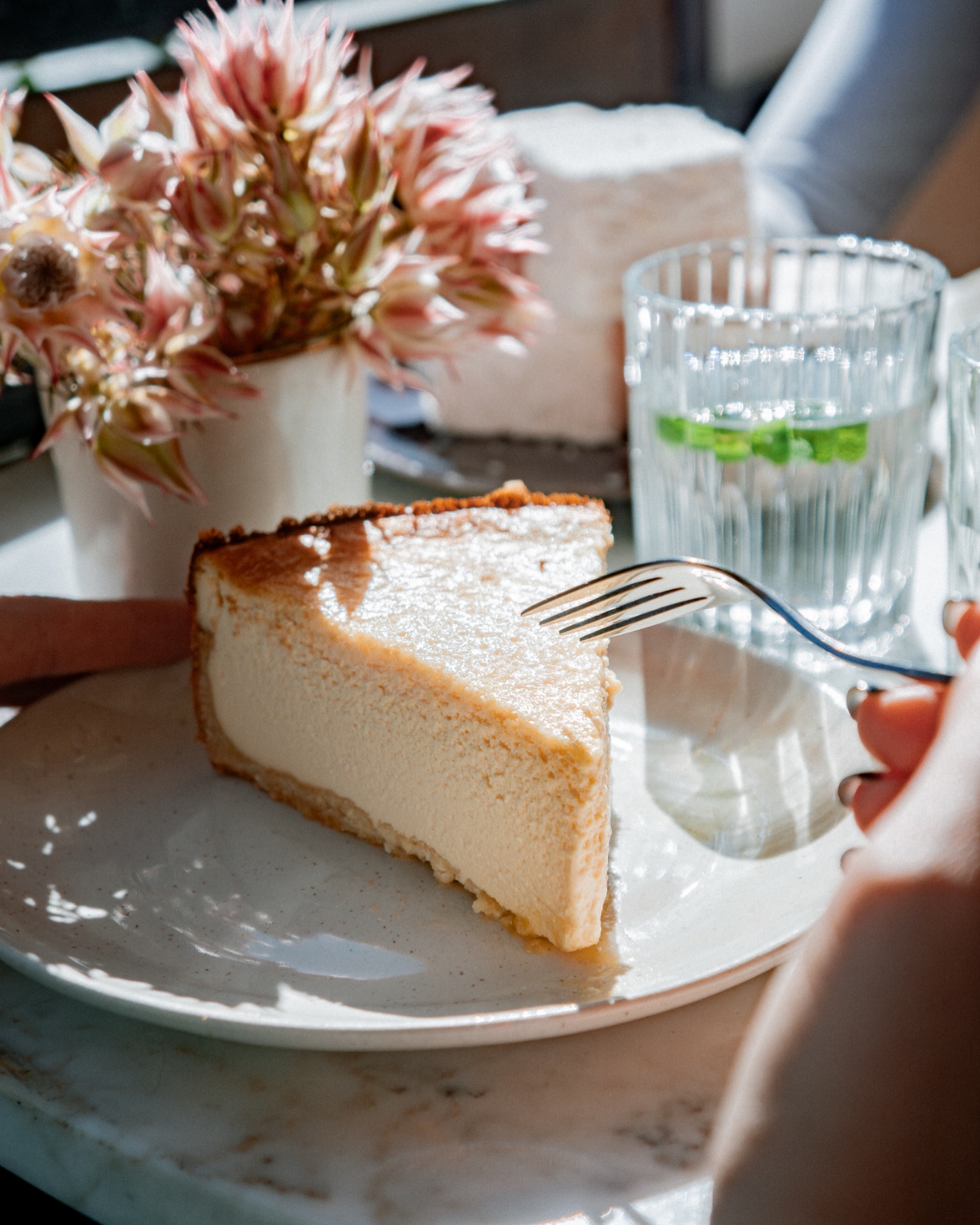 Slice of cheesecake on white plate with fork and glass of water