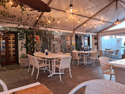 Damhuis Restaurant covered seaside dining patio with wicker tables, string lights and fishing-net decor