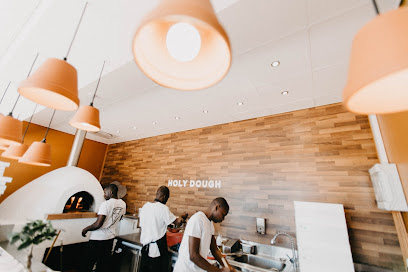 Holy Dough staff prepping at counter beneath the white HOLY DOUGH sign