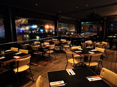Copper Club Tyger Waterfront dining room at night with set tables, chairs and waterfront lights.