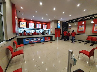 Roman's Pizza Strand interior showing counter, staff, seating and 'WE DELIVER' banner
