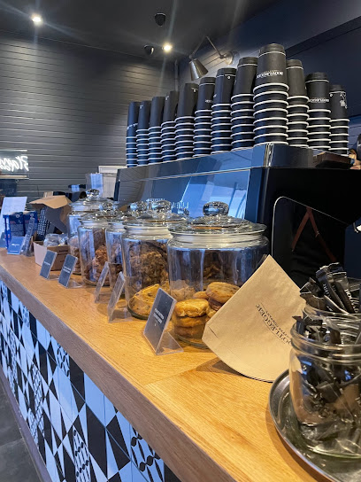 Bootlegger XS Muizenberg Halaal counter with jars of cookies and stacked takeaway cups