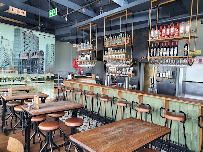 Hudsons Muizenberg dining area with wooden tables, bar stools and bottle-lined bar