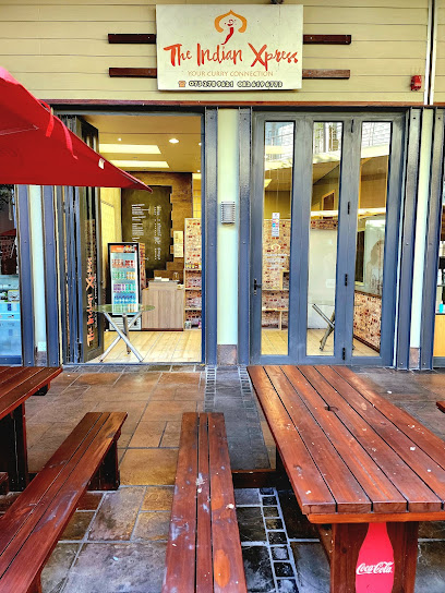 The Indian Xpress storefront with glass doors and wooden outdoor picnic tables