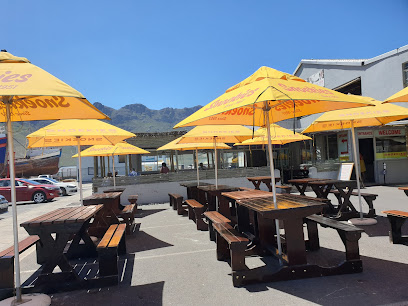 Snoekies Hout Bay outdoor picnic tables with yellow Snoekies umbrellas by the harbor