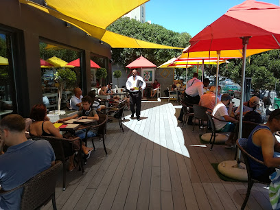 De Brasserie outdoor terrace with diners and waiter under red and yellow umbrellas