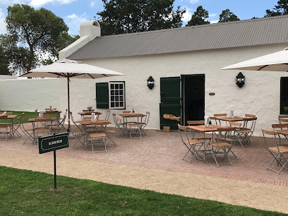 Sushi Box Constantia outdoor patio with wooden tables, umbrellas, white building and green doors.