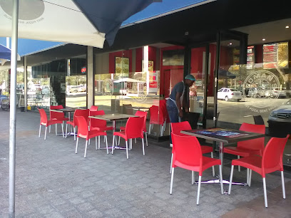 Roman's Pizza Rosmead outdoor seating with red chairs and staff at the entrance