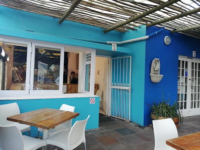 Outdoor seating and service window at Kommetjie Pizzeria with turquoise and blue walls