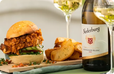 Crispy fried chicken sandwich with potato wedges beside Nederburg Sauvignon Blanc
