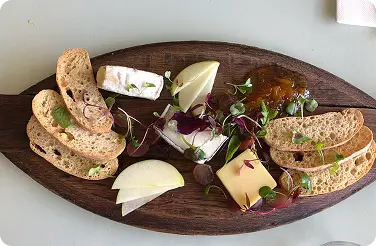 Cheese board with brie, semi-hard cheese, crostini, apple slices, honey, microgreens