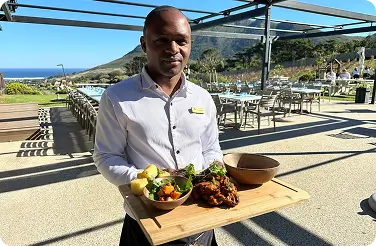 Server presenting wooden board with salad and grilled meat on outdoor terrace